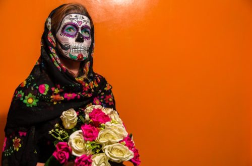 Lady with colorful sugar skull makeup and a bouquet of roses