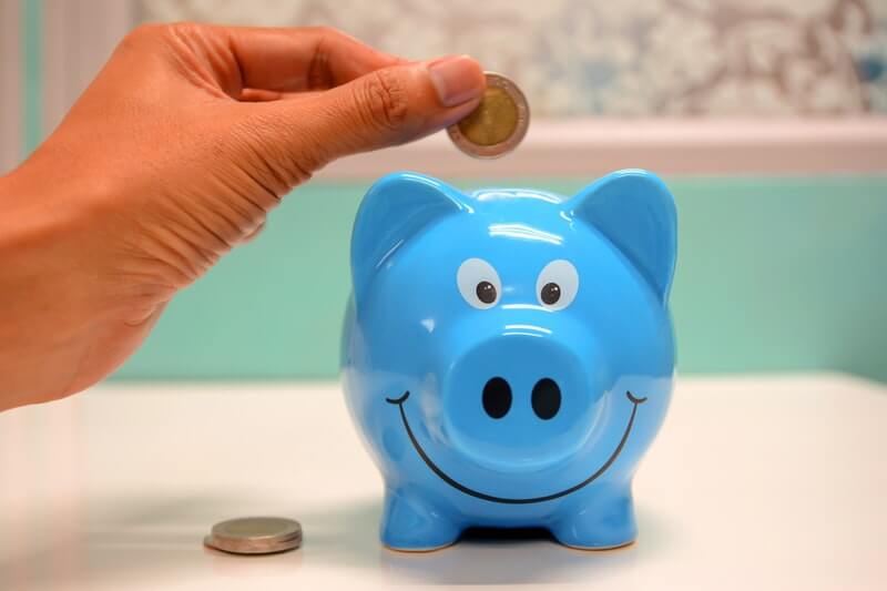Hand putting coins into a blue piggy bank